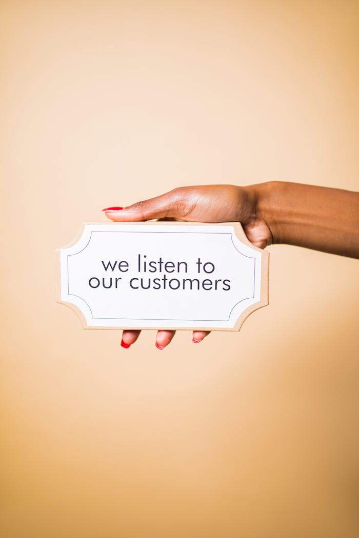 about-img A hand holding a sign saying we listen to our customers on a neutral background.